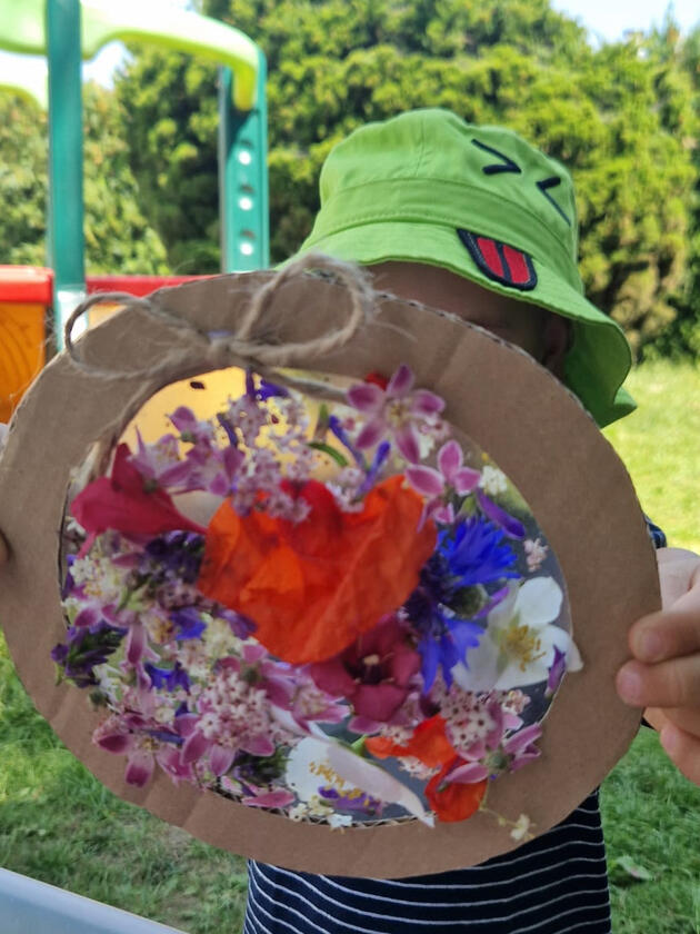 Child presenting an art project made with flowers in the garden of Mariposa Nursery