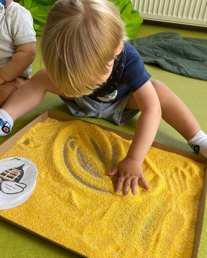 Child finger-painting on groats at Mariposa Nursery